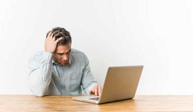Genç yakışıklı adam çalışan ile onun laptop yorgun ve çok Sleepy tutmak el üzerinde kafa.