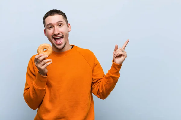 Joven Hombre Caucásico Sosteniendo Una Dona Sonriendo Alegremente Señalando Con — Foto de Stock