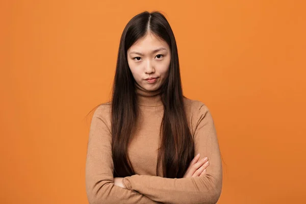 Young pretty chinese woman frowning face in displeasure, keeps arms folded.