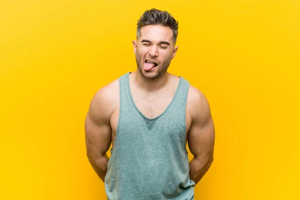 年轻的健身男子在黄色背景有趣和友好的伸出舌头 — 图库照片