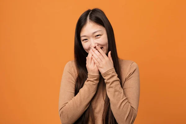 Young pretty chinese woman laughing about something, covering mouth with hands.