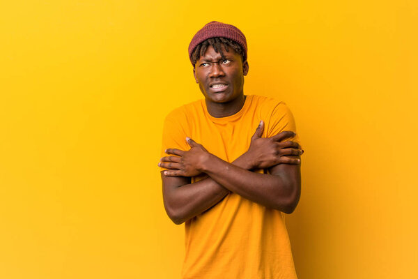 Young black man wearing rastas over yellow background going cold due to low temperature or a sickness.