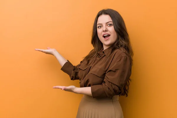 Young curvy russian woman excited holding a copy space on palm.