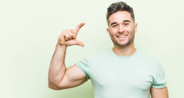 Yeşil bir arka plana karşı genç yakışıklı adam, gülme ve güven ile küçük bir şey tutan.