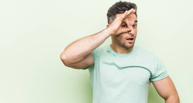 Yeşil bir arka plan karşı Genç yakışıklı adam göz ok jest tutmak heyecanlı.