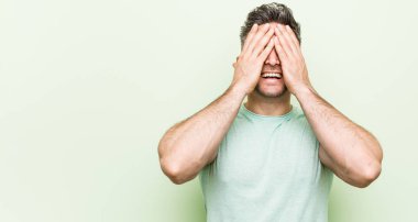 Yeşil bir arka plan karşı Genç yakışıklı adam elleri ile gözleri kapsar, geniş bir sürpriz bekliyor gülümsüyor.