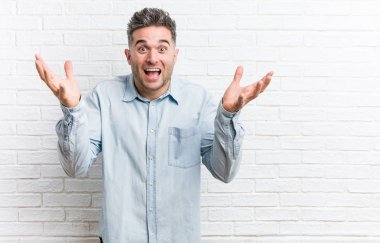 Hoş bir sürpriz alan bir tuğla duvara karşı genç yakışıklı adam, heyecanlı ve ellerini yükselterek.