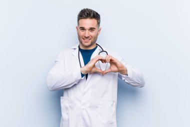 Genç yakışıklı doktor adam gülümseyen ve elleriyle bir kalp şekli gösteren.