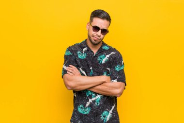 Genç filipinli adam yazlık giysiler giyen hoşnutsuzluk içinde yüz kaşlarını çatma, kollarını katlanmış tutar.