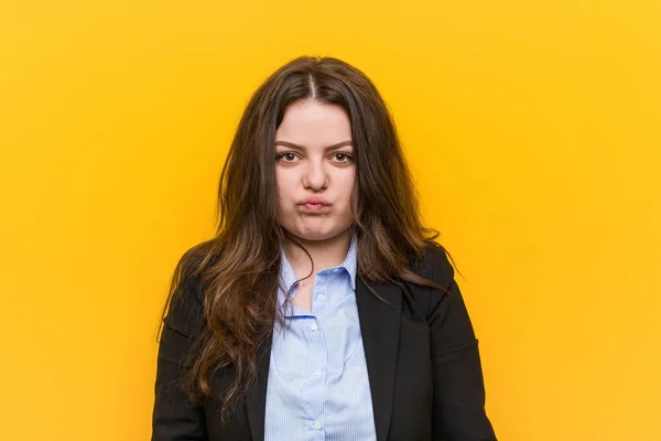 Young plus size caucasian business woman blows cheeks, has tired expression. Facial expression concept.