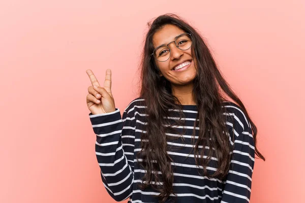 Young intellectual indian woman joyful and carefree showing a peace symbol with fingers.