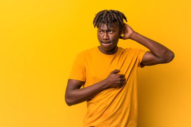 Genç siyah adam sarı arka plan üzerinde rastas giyen başının arkasına dokunmadan, düşünme ve bir seçim yapma.