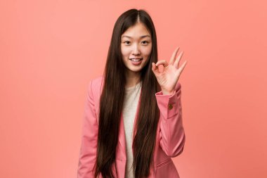 Pembe takım elbise giyen genç iş Çinli kadın ok jest gösteren neşeli ve kendinden emin.