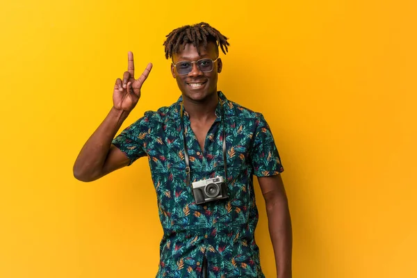 Young black rasta man wearing a vacation look showing victory sign and smiling broadly.