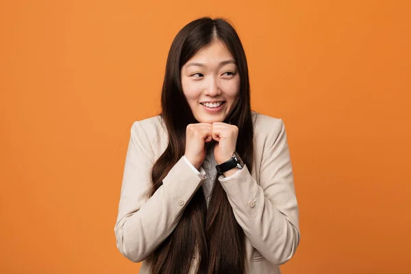 Young business chinese woman keeps hands under chin, is looking happily aside.