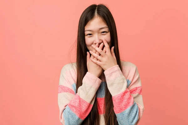 Young cool chinese woman laughing about something, covering mouth with hands.