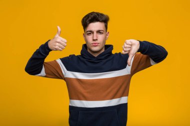 Genç serin adam başparmak yukarı ve başparmak aşağı gösteren bir kapüşonlu giyen, zor kavramı seçin