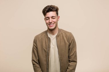 Kahverengi bir ceket giyen genç beyaz adam güler ve gözleri kapatır, rahat ve mutlu hissediyor.