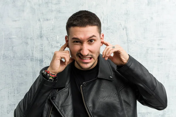 Young rocker man covering ears with his hands.