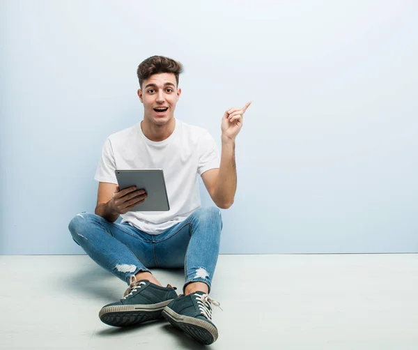 Jonge Man Met Een Tablet Zittend Indoor Glimlachend Vrolijk Wijzend — Stockfoto