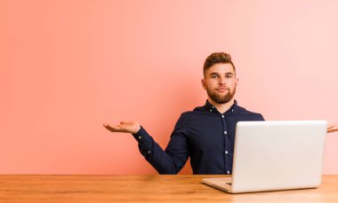 Dizüstü bilgisayarıyla çalışan genç adam kollarıyla ölçeklendiriyor, mutlu ve kendinden emin hissediyor.