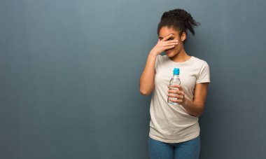 Genç siyah kadın utandı ve aynı zamanda gülüyor. Elinde bir su şişesi var..