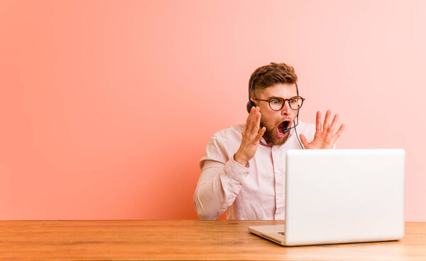 Молодой человек, работающий в колл-центре, громко кричит, держит глаза открытыми и руки напряженными
.