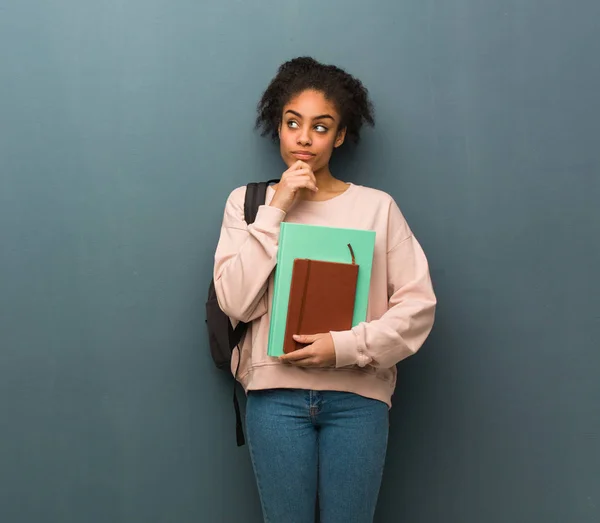 Young student black woman thinking about an idea. She is holding books.