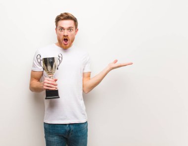 Genç kızıl saçlı adam avuç içinde bir şey tutuyor. Bir kupa tutarak.