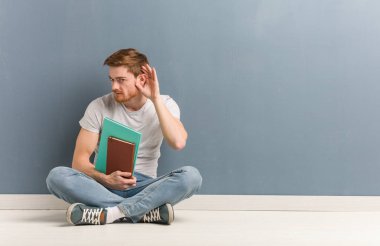 Genç kızıl saçlı öğrenci adam yerde oturan bir dedikodu dinlemeye çalışın. Elinde kitap var..