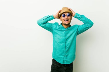 Yazlık kıyafetler giyen genç İspanyol adam sevinçle elleri başında tutarak gülüyor. Mutluluk kavramı.