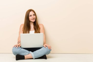 Evinin zemininde oturan genç zencefilli kadın gülümseyen, neşeli ve hoş bir kenara bakıyor.