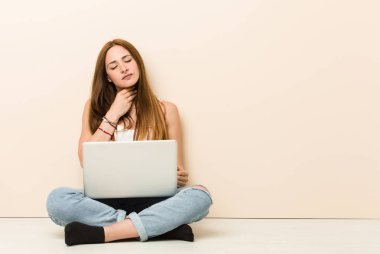 Evinin zemininde oturan genç zencefilli kadın bir virüs veya enfeksiyon nedeniyle boğaz ağrısı çekiyor.