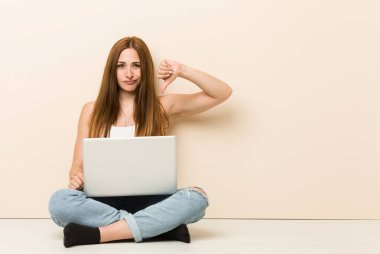 Genç zencefilli kadın evinin zemininde oturan bir nefret jesti gösteren, başparmak aşağı. Anlaşmazlık kavramı.