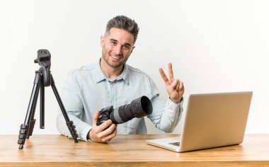 Genç yakışıklı fotoğraf öğretmeni zafer işareti gösteren ve geniş gülümseyen.