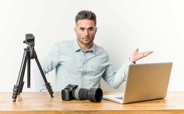 Young handsome photography teacher showing a copy space on a palm and holding another hand on waist.