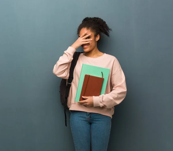Young student black woman embarrassed and laughing at the same time. She is holding books.