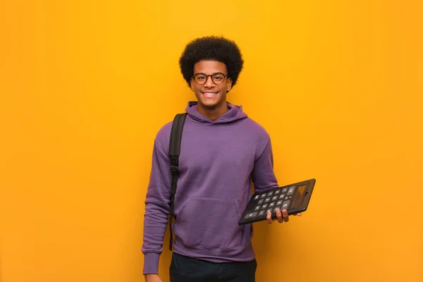 Young african american student man holding a calculator cheerful with a big smile
