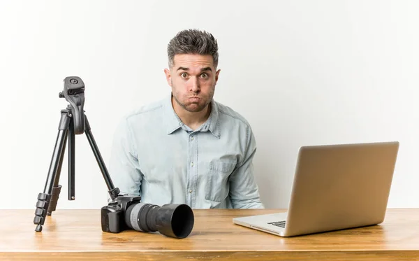 Young handsome photography teacher blows cheeks, has tired expression. Facial expression concept.