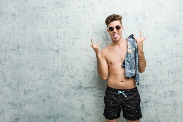 Parmaklarıyla kaya hareketi gösteren mayo giyen beyaz genç adam