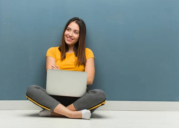 ノートパソコンを持って床に座る若い女性は 自信を持って笑顔で腕を組み 見上げる — ストック写真