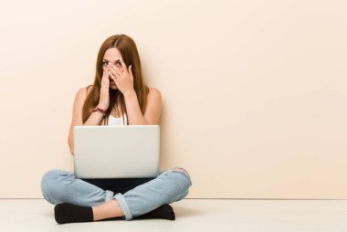 Evinin zemininde oturan genç zencefilli kadın korkmuş ve gergin parmakları ile göz kırptı.