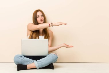 Genç zencefil kadın iki eliyle bir şey tutarak evinin zemininde oturan, ürün sunumu.