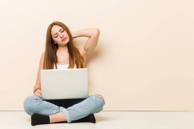 Genç zencefilkadın evinin zemininde başının arkasına dokunarak, düşünme ve bir seçim yapma oturuyor.