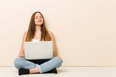 Evinin zemininde oturan genç zencefilli kadın karına dokunur, hafifçe gülümser, yemek ve tatmin kavramı.