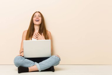 Evinin zemininde oturan genç zencefilli kadın yüksek sesle göğüs üzerinde el tutmak dışarı gülüyor.