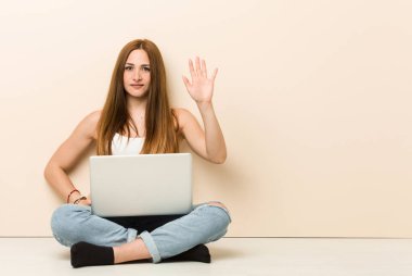 Genç zencefil kadın evinin zemininde otururken neşeli gülümseyerek parmakları ile beş numara gösteren.