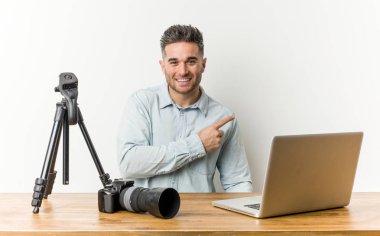 Genç yakışıklı fotoğraf öğretmeni gülümseyerek ve bir kenara işaret, boş alanda bir şey gösteren.