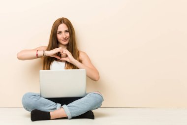 Genç zencefil kadın evin in katta gülümseyerek oturan ve elleriyle bir kalp şekli gösteren.