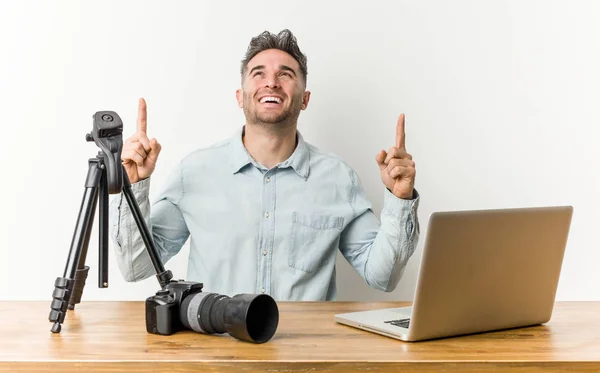 Young handsome photography teacher indicates with both fore fingers up showing a blank space.